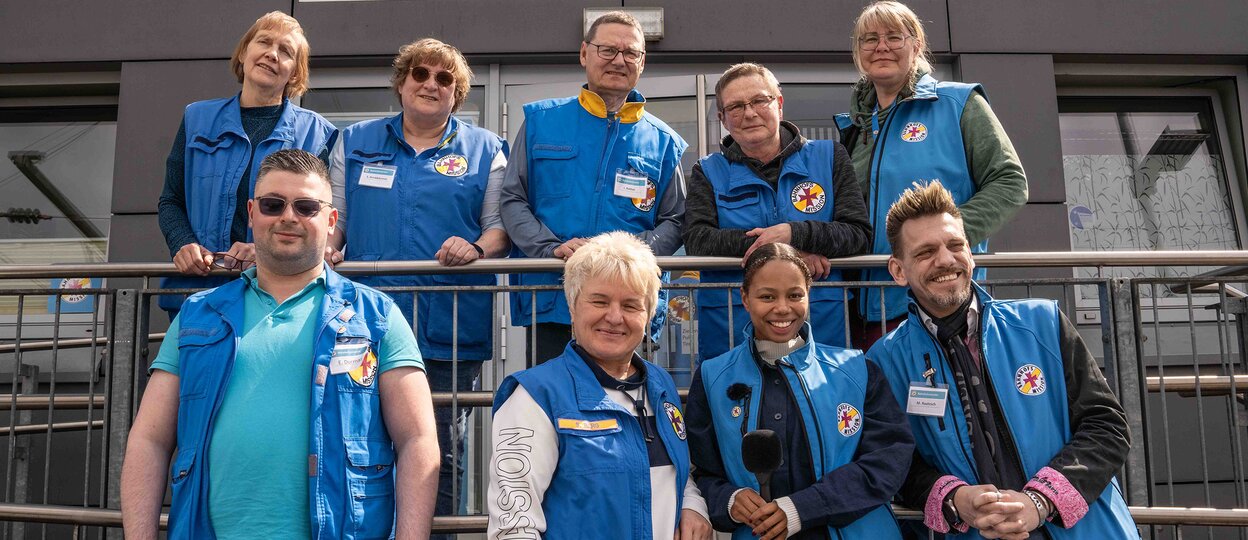 Das Team der Bahnhofsmission steht vor der Tür der Bahnhofsmission und schaut in die Kamera. Das Team der Bahnhofsmission steht vor der Tür der Bahnhofsmission und schaut in die Kamera.